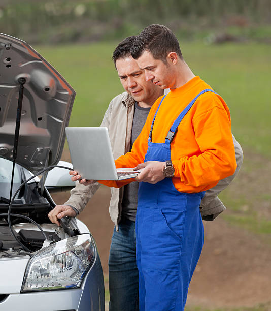 mechanic on roadside works with customer on laptop computer.