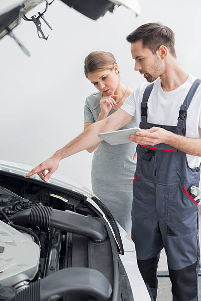 young repair worker explaining car engine to worried customer in workshop